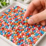 Bunte Thermostar® Sensory Beads Stone aus Silikon werden mit einem weißen Löffel aus einem Tablett aufgenommen