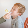 Kind bei logopädischer Übung mit TalkTools® Horn Nr. 12 in Gelb – Atem- und Mundmotoriktraining