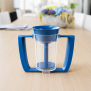 TotalCup® Trinkbecher mit Dosiereinsatz im Einsatz auf einem Tisch in einer Pflege- oder Therapiesituation