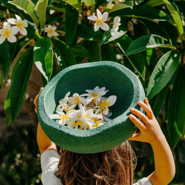 Kind trägt einen grünen Stapelstein mit weißen Blumen im Garten – Spiel und Natur entdecken.