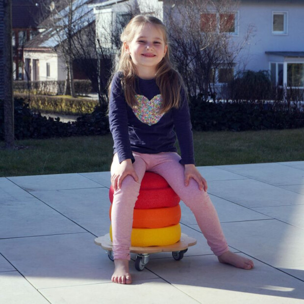 Anwendungsbild 2: Kind nutzt den Pedalo® Rollflitzer mit mehreren Stapelsteinen als fahrbare Sitzfläche im Innenbereich.